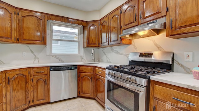 kitchen featuring stainless steel appliances, under cabinet range hood, a sink, brown cabinets, and tasteful backsplash