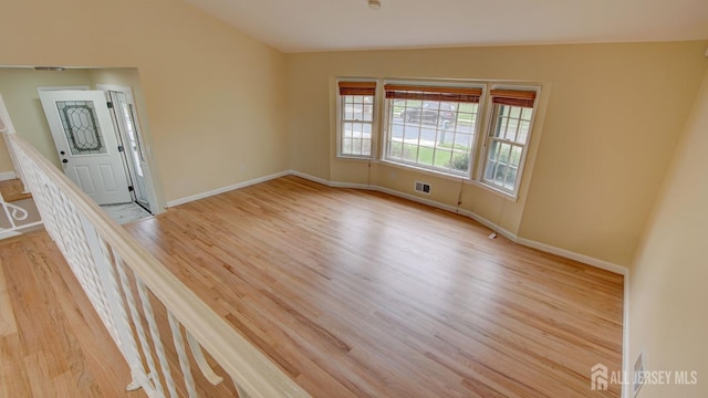 spare room featuring light wood finished floors, visible vents, and baseboards