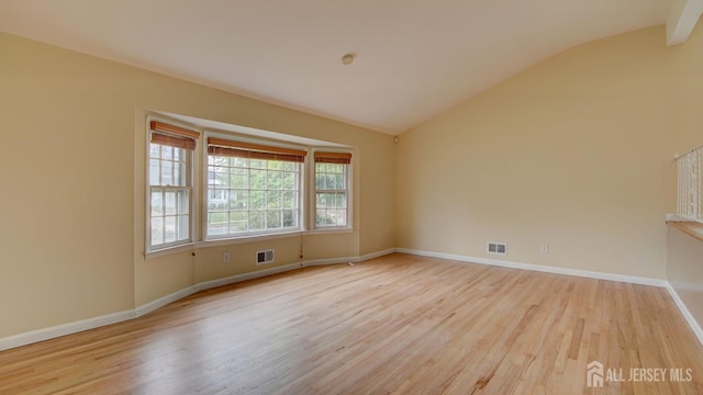 empty room featuring lofted ceiling, baseboards, visible vents, and wood finished floors