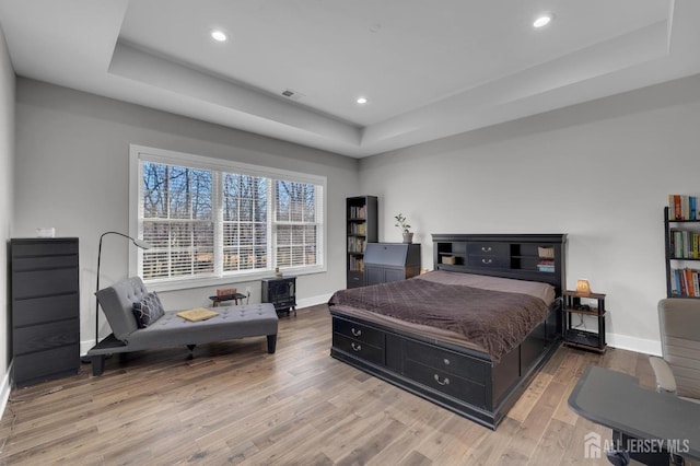 bedroom with a tray ceiling, wood finished floors, and baseboards