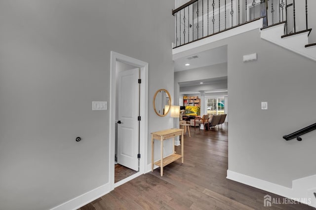 corridor featuring a towering ceiling, stairway, baseboards, and wood finished floors