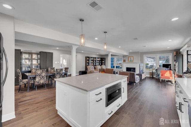 kitchen with stainless steel microwave, visible vents, open floor plan, dark wood-style floors, and ornate columns