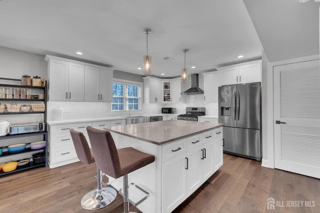 kitchen featuring stainless steel appliances, wood finished floors, wall chimney exhaust hood, and white cabinetry