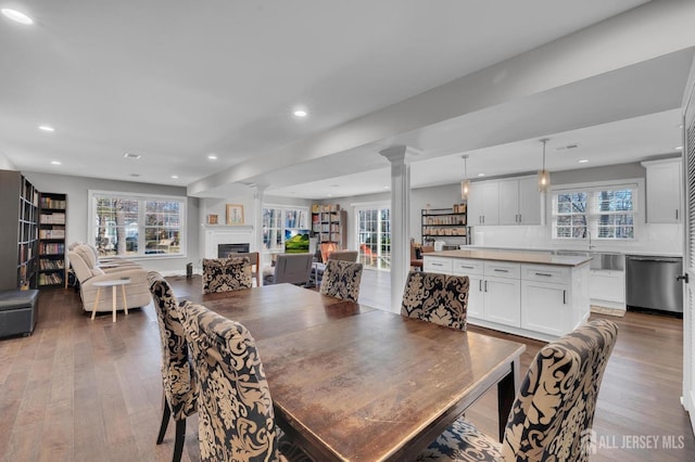 dining room with plenty of natural light, wood finished floors, a fireplace, and ornate columns