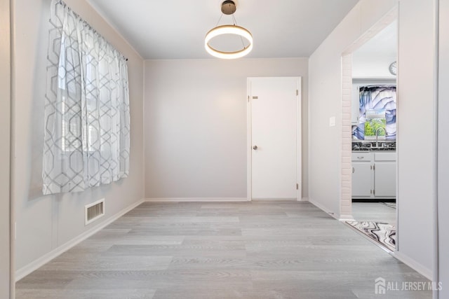 hallway with a sink, baseboards, light wood-type flooring, and visible vents