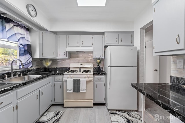 kitchen with a sink, white appliances, tasteful backsplash, under cabinet range hood, and dark countertops