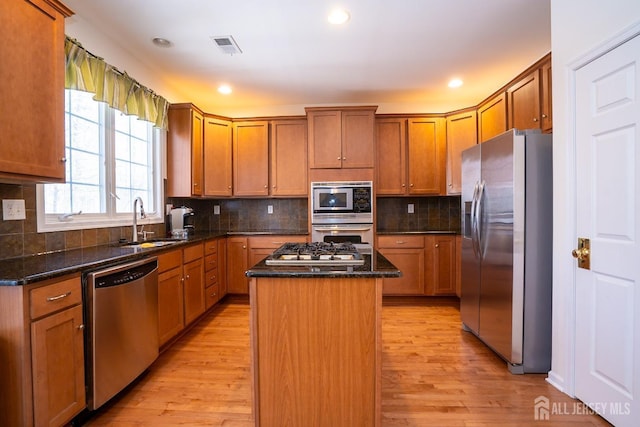 kitchen featuring stainless steel appliances, light wood-style flooring, a sink, a kitchen island, and dark stone counters