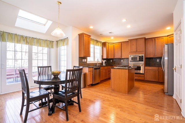 kitchen featuring a center island, a skylight, dark countertops, appliances with stainless steel finishes, and a sink