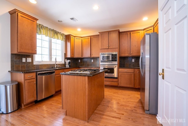 kitchen with a sink, a kitchen island, visible vents, appliances with stainless steel finishes, and light wood finished floors