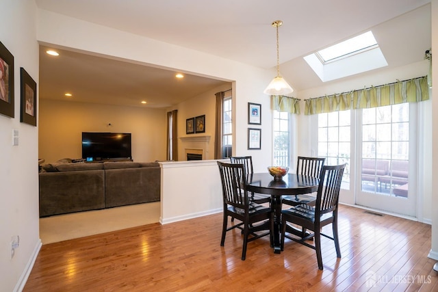 dining room featuring hardwood / wood-style flooring, a skylight, a fireplace, and visible vents