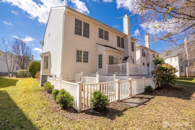 rear view of property featuring a lawn, a chimney, and a wooden deck