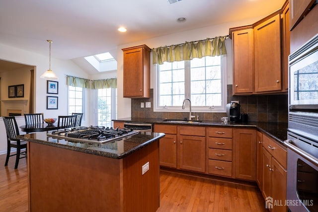 kitchen featuring vaulted ceiling with skylight, stainless steel appliances, a sink, light wood-style floors, and brown cabinetry