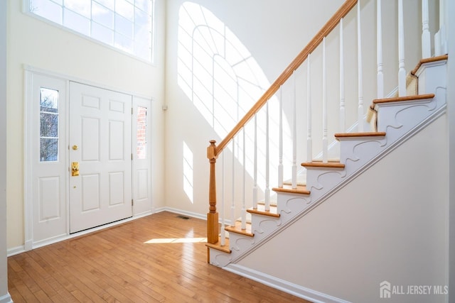 entryway featuring visible vents, hardwood / wood-style floors, a high ceiling, and baseboards