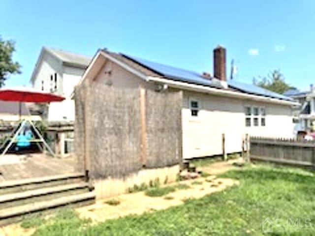 rear view of property with a wooden deck, a yard, and solar panels