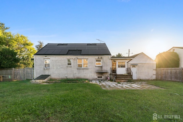 rear view of house with roof mounted solar panels, a lawn, and a fenced backyard