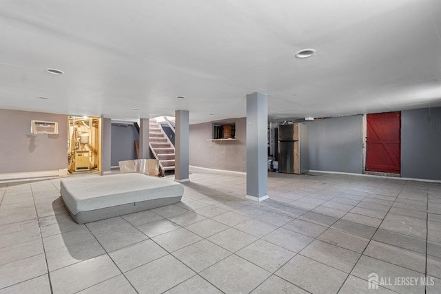 finished basement featuring a wall mounted air conditioner, stairway, light tile patterned floors, and freestanding refrigerator