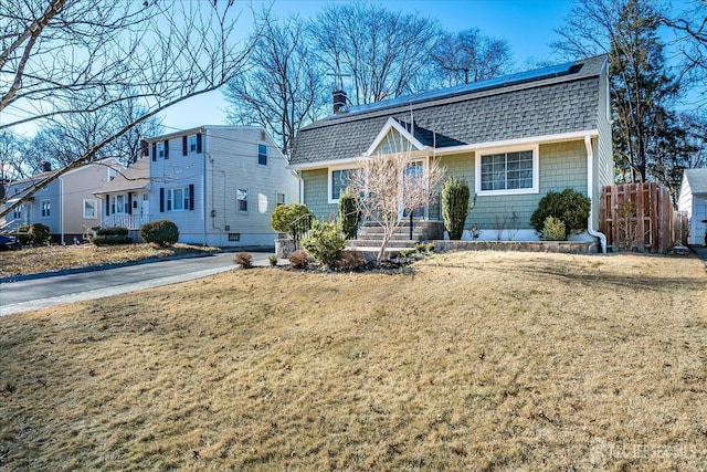 dutch colonial with roof mounted solar panels, fence, a front lawn, and roof with shingles