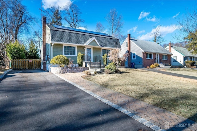 dutch colonial featuring solar panels, fence, roof with shingles, a front lawn, and a chimney