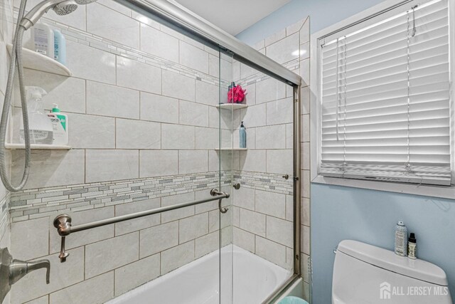 bathroom with toilet and shower / bath combination with glass door