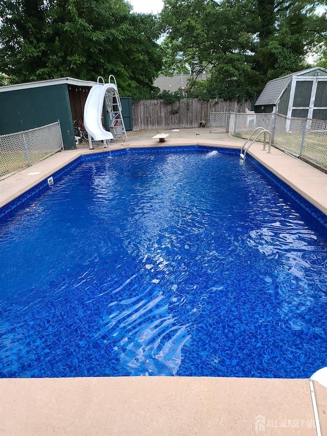 view of swimming pool with a diving board, fence, a water slide, and a fenced in pool