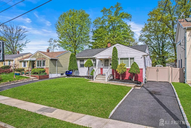 bungalow-style house with aphalt driveway, brick siding, a front yard, a gate, and a chimney