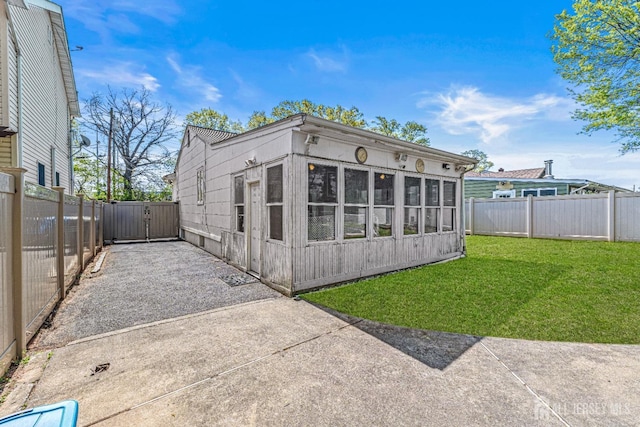 rear view of property featuring a lawn, a gate, a sunroom, a patio area, and a fenced backyard