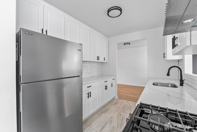 kitchen with sink, white cabinets, light stone counters, decorative backsplash, and stainless steel refrigerator