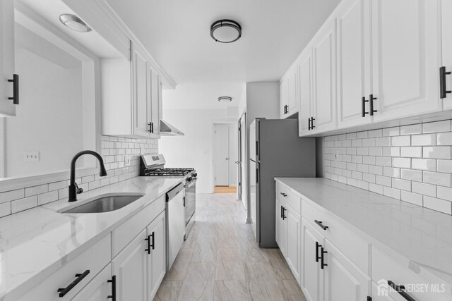 kitchen featuring white cabinets, stainless steel appliances, light stone counters, decorative backsplash, and sink