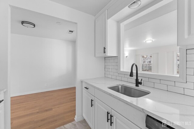 kitchen with dishwasher, white cabinetry, light stone countertops, sink, and light hardwood / wood-style flooring