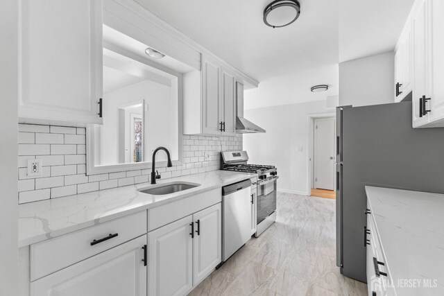 kitchen featuring appliances with stainless steel finishes, light stone counters, decorative backsplash, white cabinets, and sink