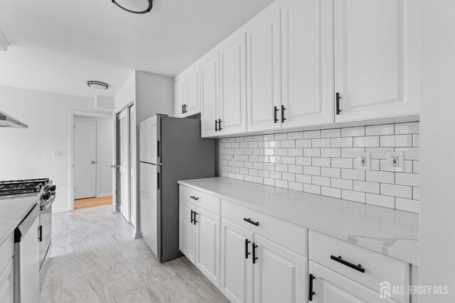 kitchen featuring light stone counters, appliances with stainless steel finishes, decorative backsplash, and white cabinetry