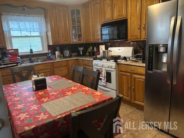 kitchen with stainless steel fridge, brown cabinets, gas range gas stove, black microwave, and backsplash