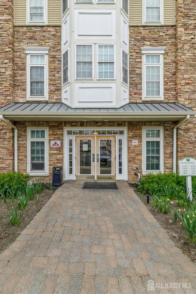 1109 Cedar Village Blvd, East Brunswick, NJ 08816 - view of exterior entry with a standing seam roof, stone siding, and metal roof
