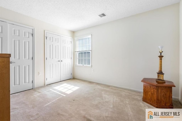 unfurnished bedroom with a textured ceiling, visible vents, and carpet