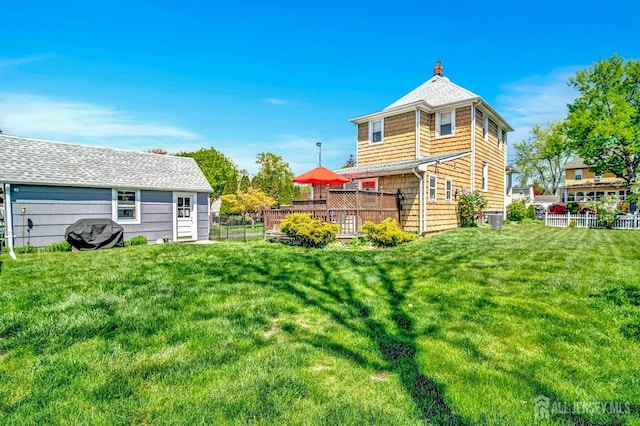 back of house with central AC, a wooden deck, fence, roof with shingles, and a lawn