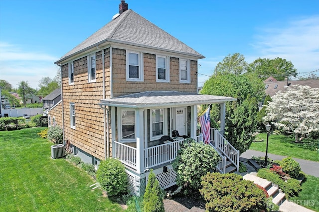 view of front facade with covered porch, a chimney, roof with shingles, and a front lawn