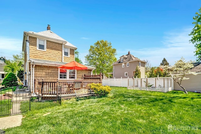back of property featuring a wooden deck, fence, a chimney, a shingled roof, and a yard