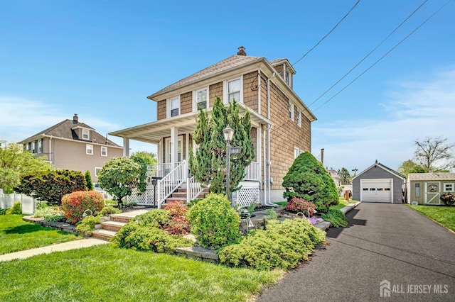 view of front of home featuring a front lawn, a detached garage, an outbuilding, covered porch, and driveway