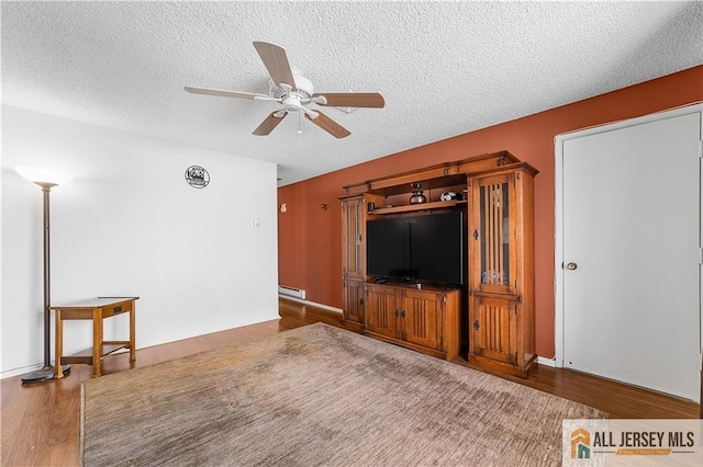 unfurnished living room featuring baseboard heating, wood finished floors, a ceiling fan, and a textured ceiling