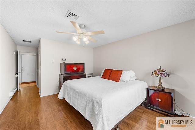 bedroom featuring visible vents, a ceiling fan, a baseboard heating unit, a textured ceiling, and wood finished floors