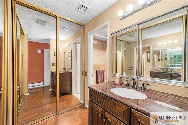 bathroom with visible vents, vanity, a baseboard heating unit, and wood finished floors