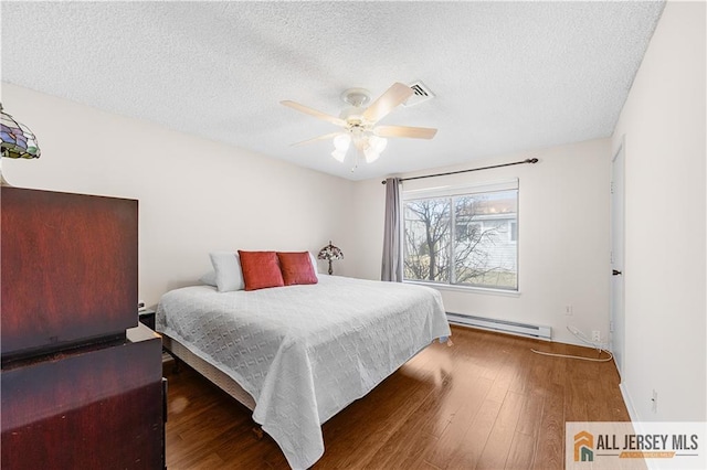 bedroom with a baseboard radiator, a textured ceiling, visible vents, and wood finished floors