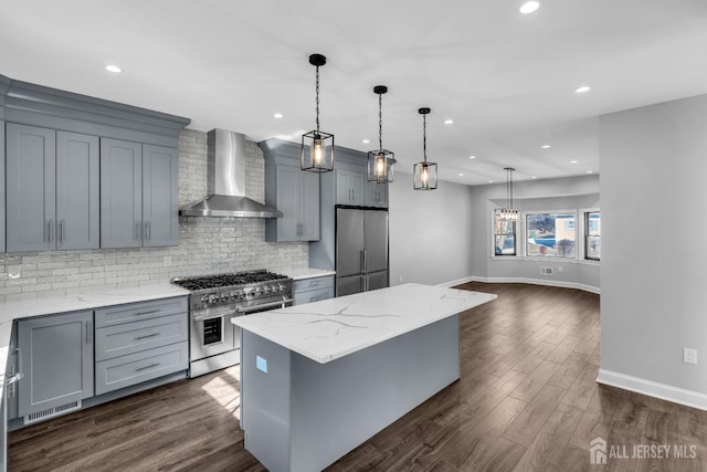 kitchen with wall chimney exhaust hood, a kitchen island, light stone counters, hanging light fixtures, and stainless steel appliances