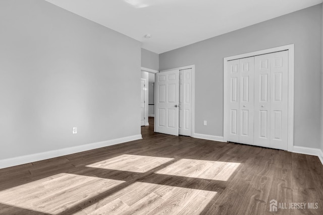 unfurnished bedroom with baseboards, dark wood-type flooring, and two closets