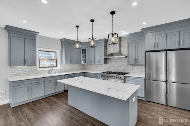 kitchen with a kitchen island, decorative light fixtures, light stone countertops, stainless steel appliances, and wall chimney range hood