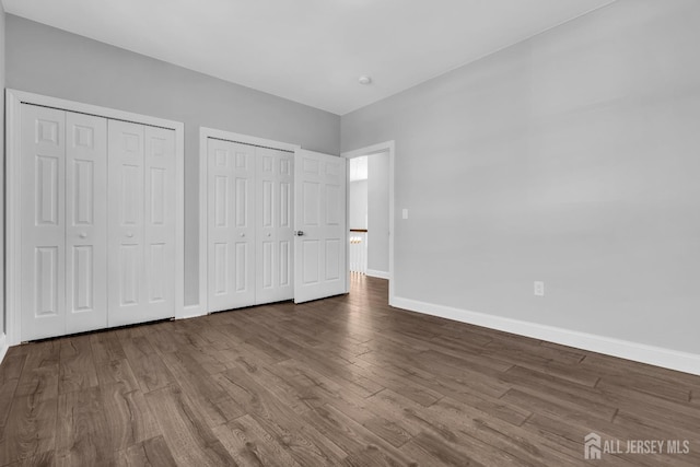 unfurnished bedroom featuring baseboards, wood finished floors, and multiple closets