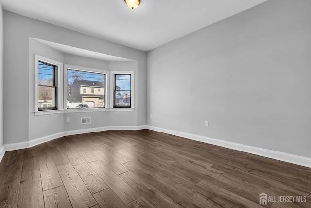 empty room with dark wood-style flooring, visible vents, and baseboards