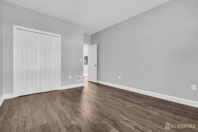 unfurnished bedroom featuring a closet, dark wood finished floors, visible vents, and baseboards