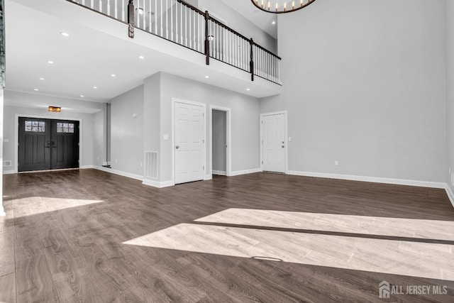 unfurnished living room with a notable chandelier, a high ceiling, baseboards, and wood finished floors