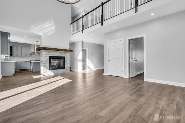 unfurnished living room with a stone fireplace, dark wood-type flooring, a high ceiling, and baseboards